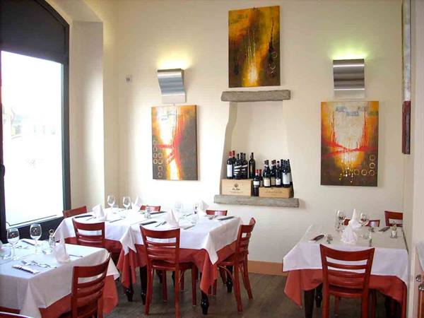 Restaurant dining room with set tables, white tablecloths, red chairs and wine bottles