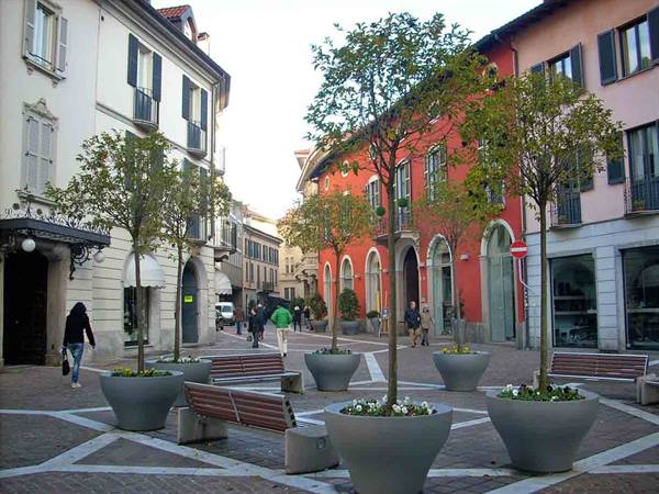 Square with trees in large concrete planters, benches and colorful buildings, people strolling