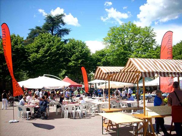 People seated at white tables under umbrellas in a sunny square
