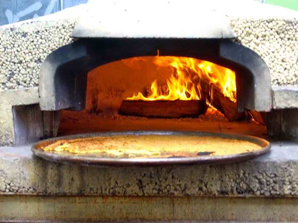 Stone wood-fired oven with blazing flames and a pizza tray