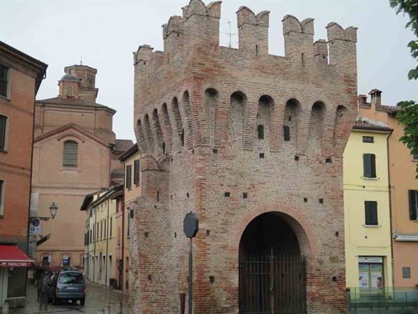 Medieval brick gate with battlements and arched entrance barred by iron gate