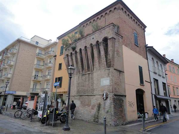 Old brick tower house with protruding arches, bicycles and pedestrians on street