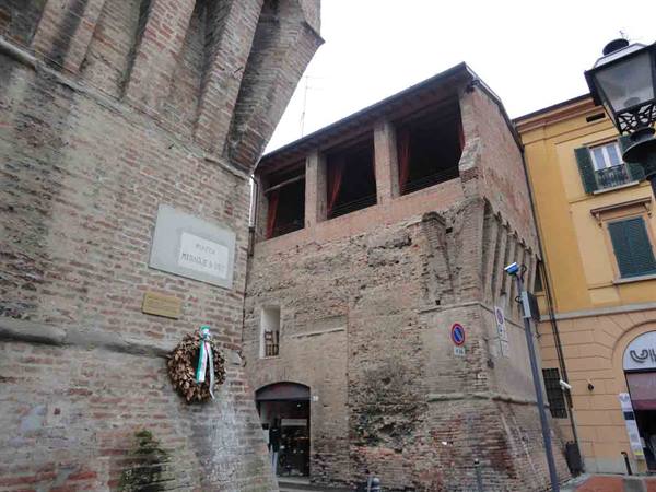 Medieval brick towers with overhangs beside yellow buildings under grey sky