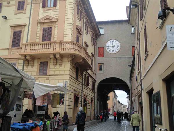 Street market below the clock tower arch in Ravenna, people walking by