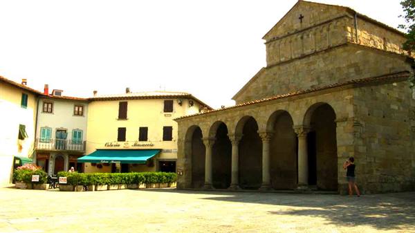 Romanesque stone church with arched portico, woman photographing nearby