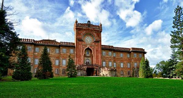 Sammezzano Castle, red brick facade with clock, green lawn and pines