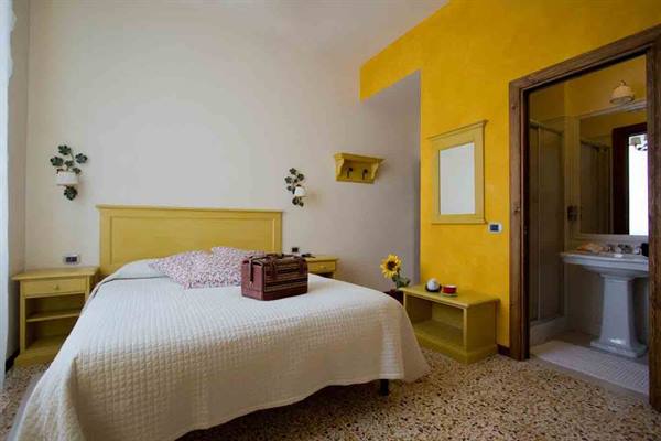 Hotel room with yellow bed, leather suitcase, yellow wall and open bathroom
