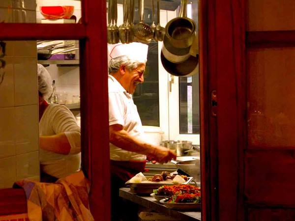 Chef in white hat plating food, seen through a red doorway