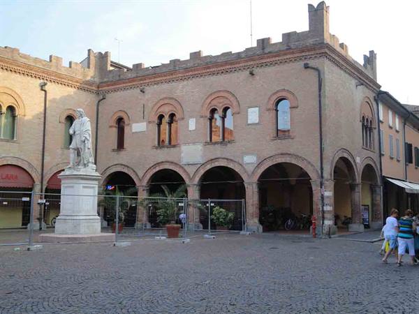 Marble statue in front of a medieval brick building with arches and battlements