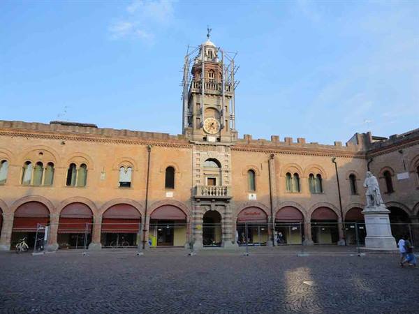 Brick palace square with clock tower under scaffolding and statue