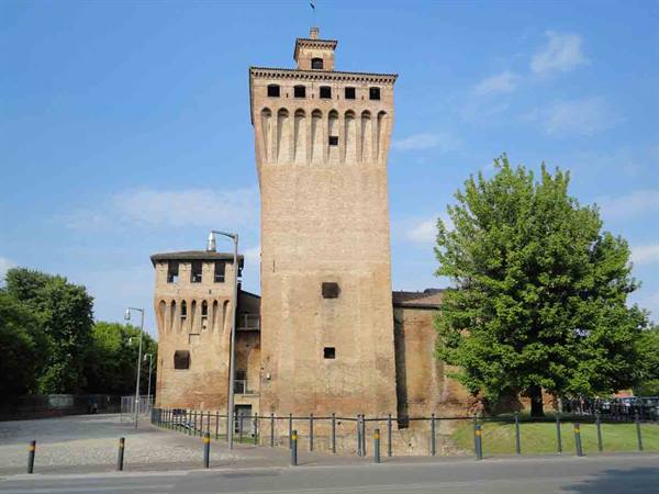 Brick tower of Rocca di Cento under blue sky, green trees beside