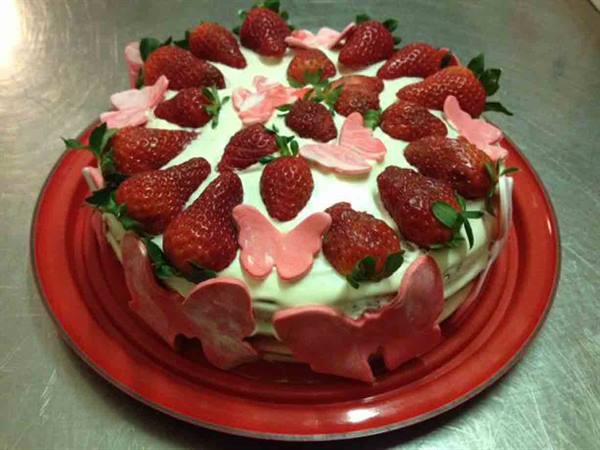 Cream cake topped with fresh strawberries and pink butterflies on red plate