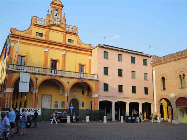 People walking in a square by an old yellow arcaded building