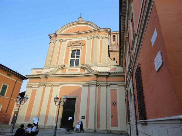 Pink and ochre baroque church facade, people sitting in the square