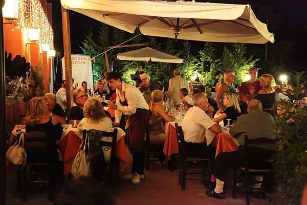Waiter serving guests at the lit trattoria tables in the evening under umbrellas