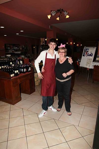 Waiter in red apron hugging a woman in a restaurant among wine bottles
