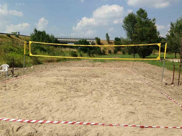 Beach volleyball court with yellow net, sand and red-white boundary tape