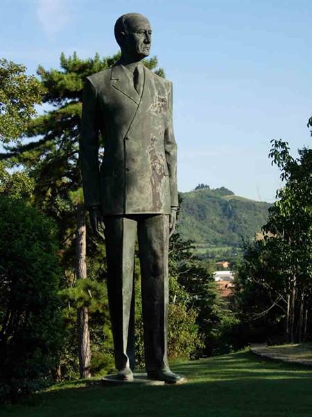 Bronze statue of a man in a suit, on a lawn among trees and hills