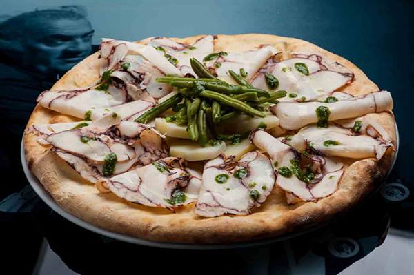 Pizza topped with octopus, potatoes and pesto in cool kitchen light