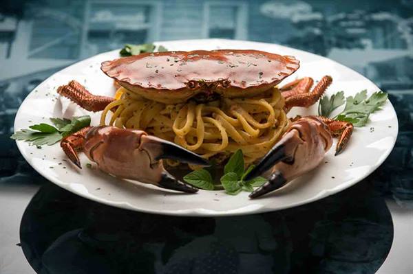 Whole crab spaghetti with claws and parsley on a white plate