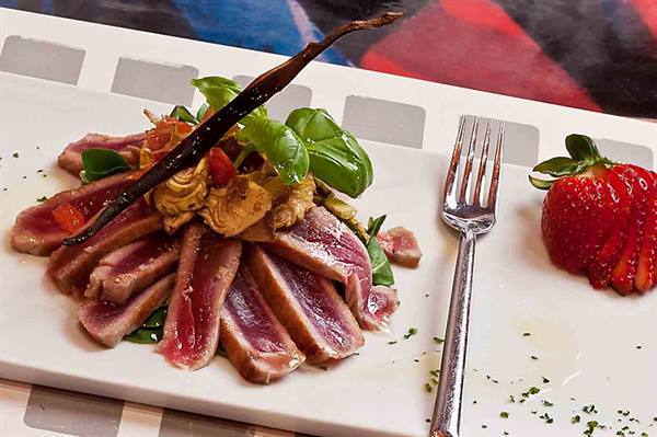 Sliced seared tuna on white plate with basil, artichokes and strawberry