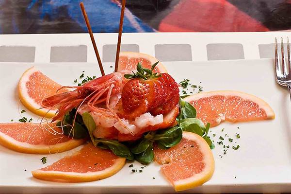 White plate with red prawn, strawberry, grapefruit slices and arugula