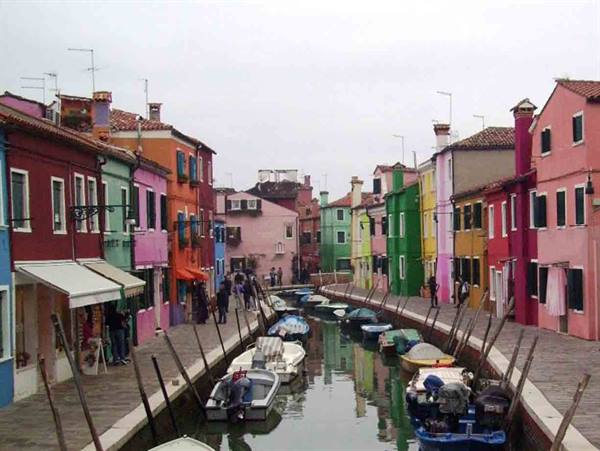 Burano canal lined with colorful houses and moored boats under grey sky