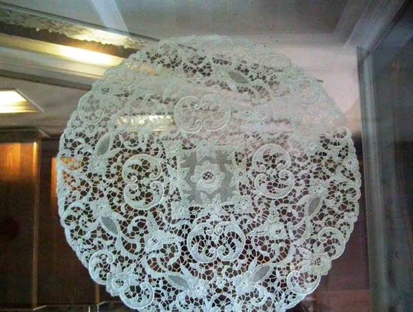 Round white lace displayed behind glass with warm indoor reflections