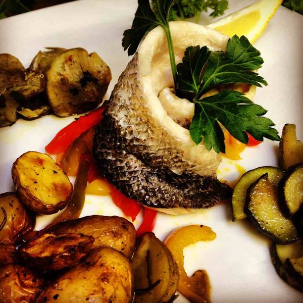 Fish fillet with roasted potatoes, zucchini and peppers on white plate