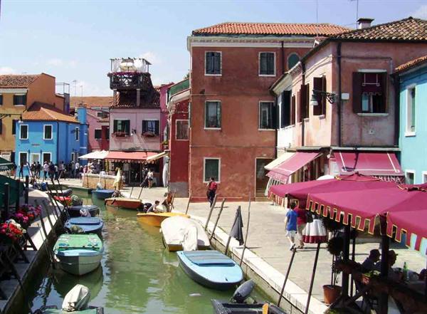 Colorful boats moored along a Burano canal among pink and blue houses