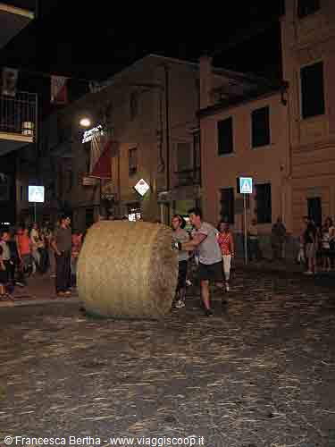Men roll a giant hay bale along a cobbled street at night