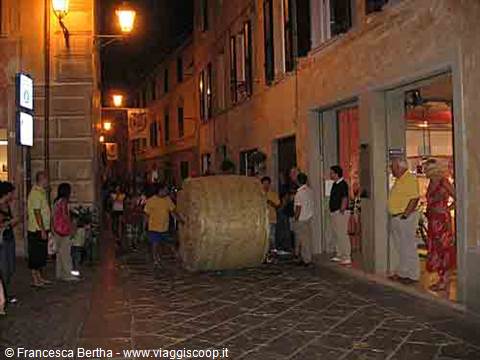 Night in the old town: crowd pushing a giant cheese wheel down the cobbled street