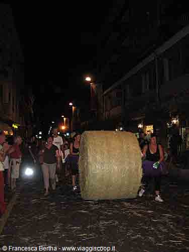 People push a giant hay bale along a street at night