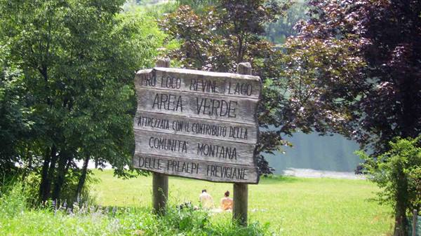 Wooden sign Area Verde, green lawn and Revine lake behind the trees