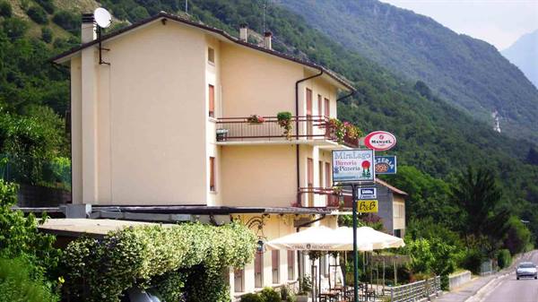Miralago hotel with sign and umbrellas beside the road, green mountain behind