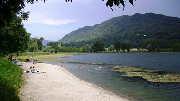 Swimmers on the sandy lakeshore, forested mountains in the background