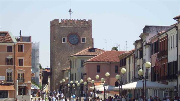 People stroll along the street past the brick clock tower in Chioggia