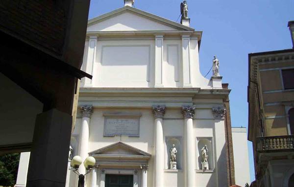 White church facade with Corinthian columns and statues, between buildings, blue sky