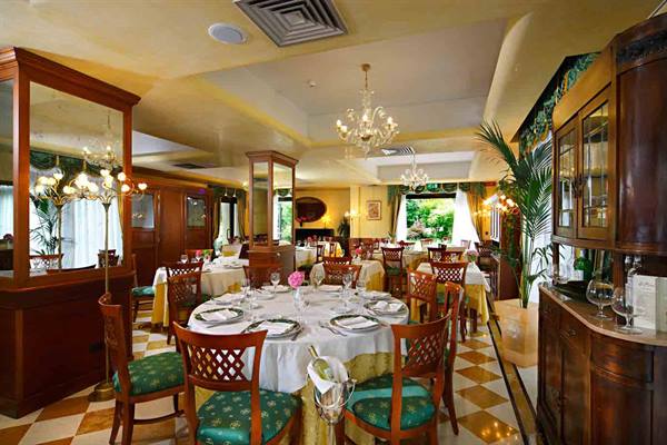 Elegant restaurant dining room with set tables, green chairs, glass chandeliers and checkered floor