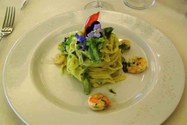 Green tagliatelle with shrimp and edible flowers on a white plate
