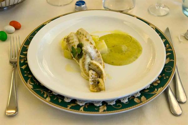 White plate with boiled fish and green sauce, paper napkin on top