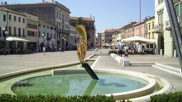 Pedestrian square with round fountain and golden sculpture on black base, café umbrellas