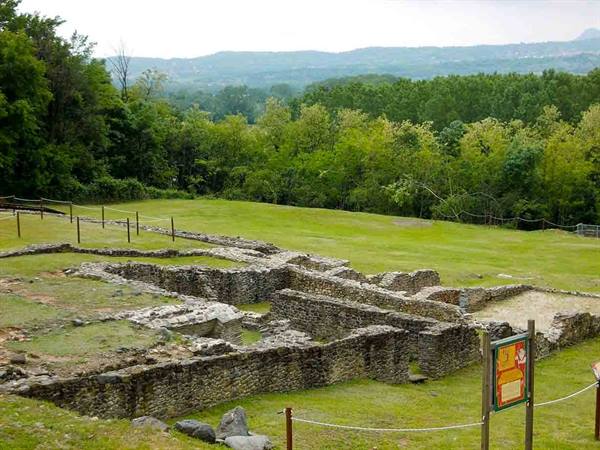 Ancient stone ruins amid green lawns and woods, hills in the background