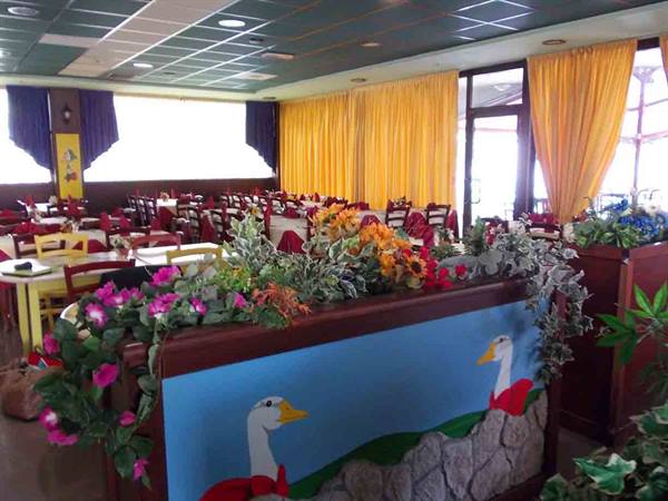 Restaurant dining room with set tables, yellow curtains and flowers