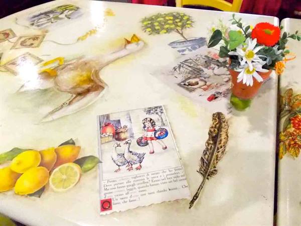 Decorated table with duck, lemons, feather, illustrated postcard and small flower pot