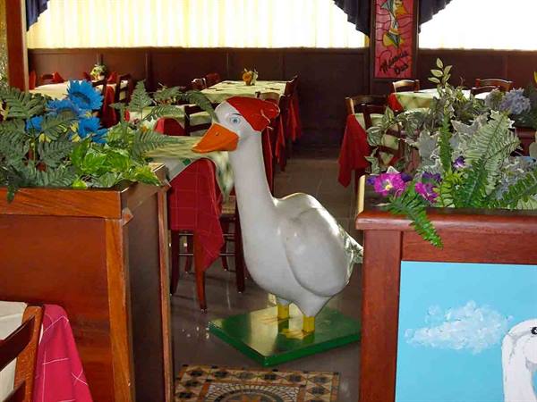 White duck statue wearing a red hat among flowers in a restaurant