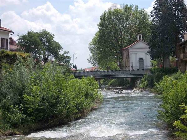River with white rapids among green bushes, bridge and small white church