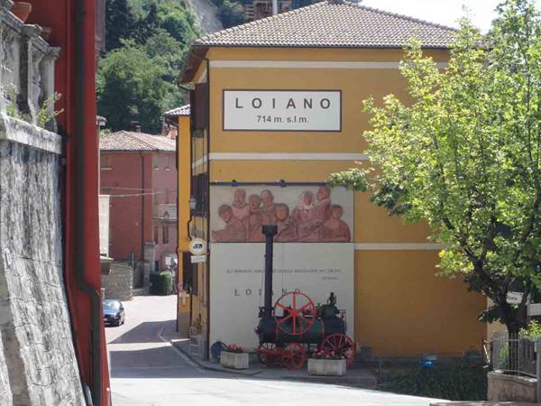 Loiano, yellow building with sign and mural, old red steam locomotive below