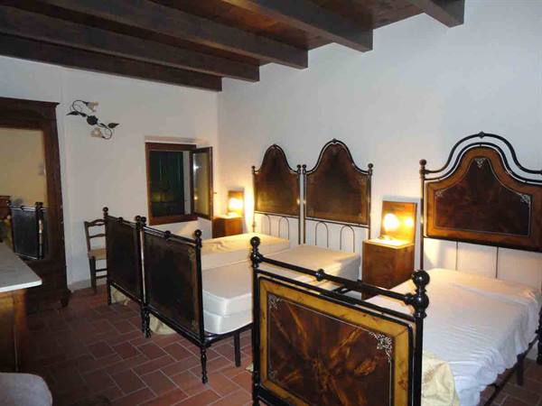 Bedroom with wrought iron and wood beds, warm lamps, terracotta floor, wooden beams