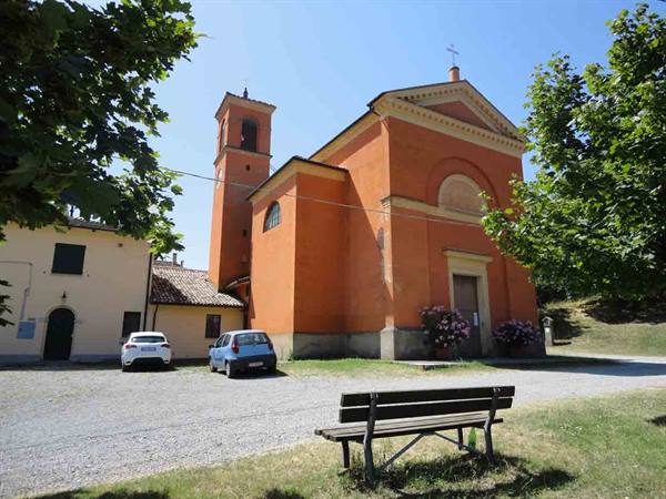 Orange church with bell tower, wooden bench and parked cars under sunny sky